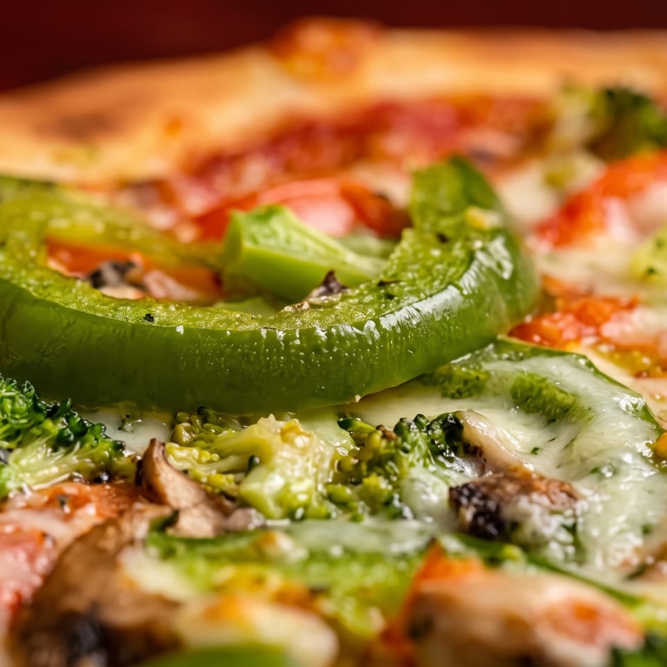 Close-up of a vegetable pizza with green bell pepper, broccoli, mushrooms, and melted cheese.